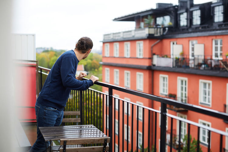 Man standing in balcony by building at urban rental apartment