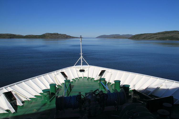 Cropped image of boat overlooking blue sea and mountains against clear sky