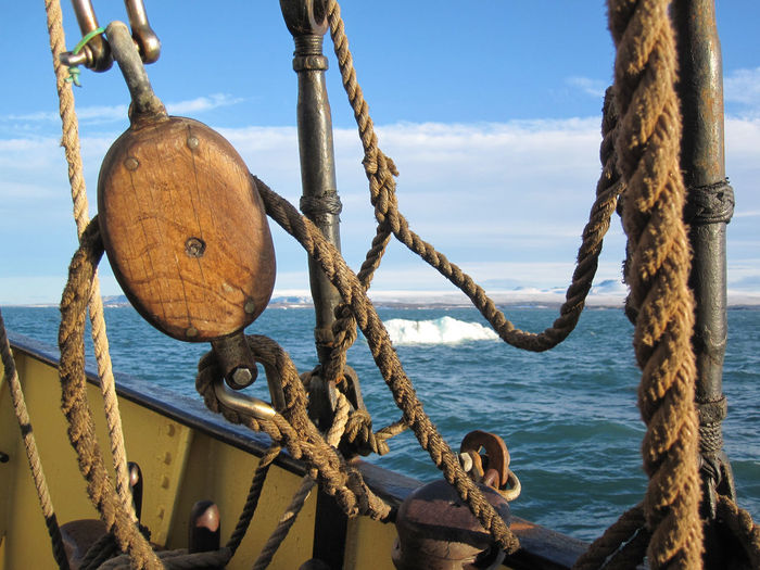 Close-up of rope tied on metal chain by sea against sky