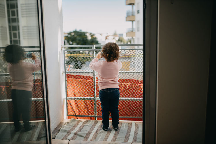 Rear view of child taking picture on balcony