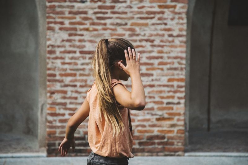 Side view of girl walking against brick wall