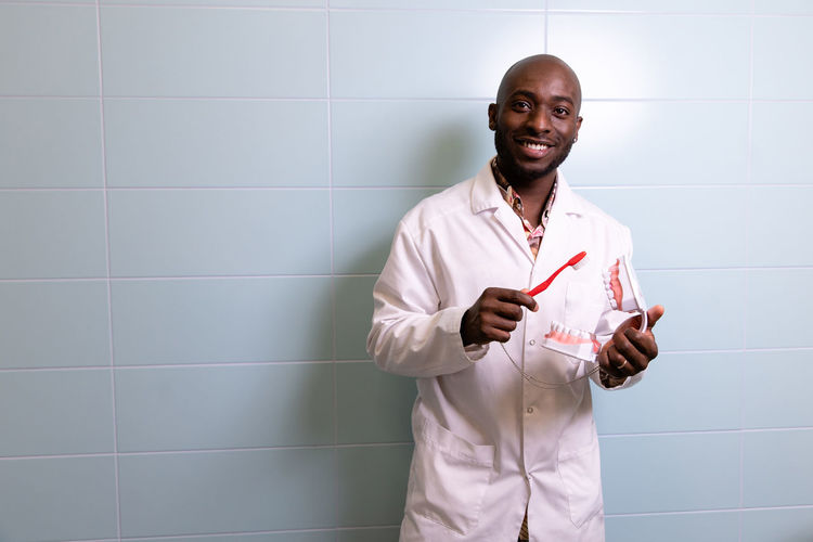 Portrait of dentist standing against wall