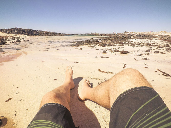 Low section of man relaxing at sandy beach on sunny day