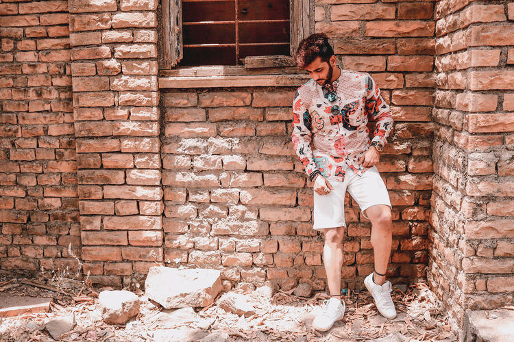 Young man looking down while standing against brick wall
