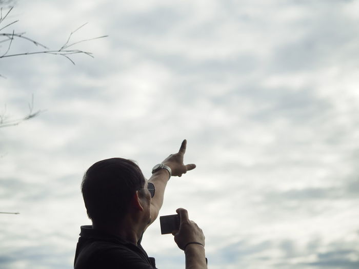 Low angle view of man holding camera while showing cloudy sky