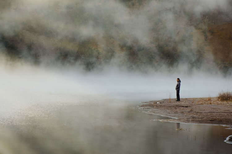 Man standing at lakeshore during foggy weather