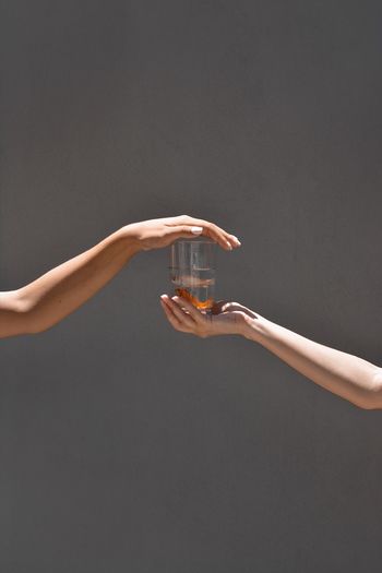 Cropped hands of people holding fish in drinking glass against gray background