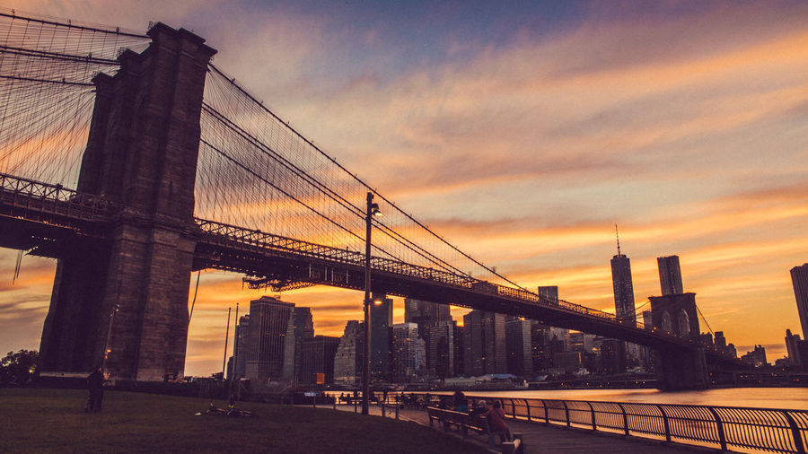 Low angle view of brooklyn bridge against cloudy sky in city during sunset