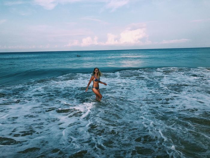 Woman wading in sea against sky