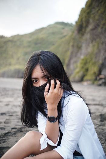 Portrait of young woman covering face with hair against mountain