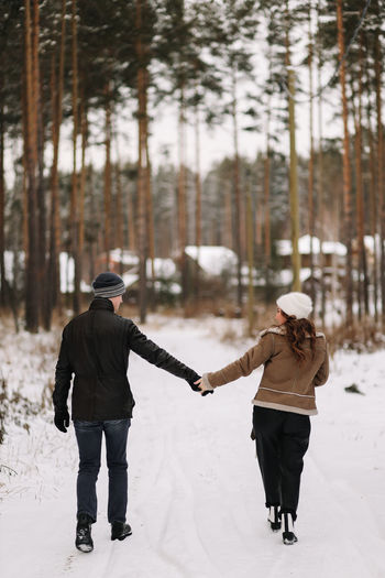 A happy couple in love in winter clothes hugging together walking in a snowy forest on an weekend