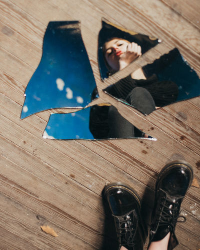 Reflection of woman in broken mirror on hardwood floor