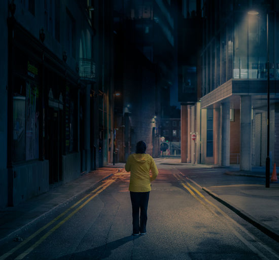 Rear view of woman walking on street amidst buildings at night