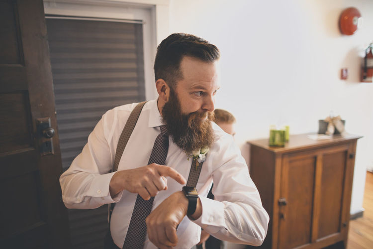 Bridegroom pointing towards wristwatch while pageboy standing behind at home