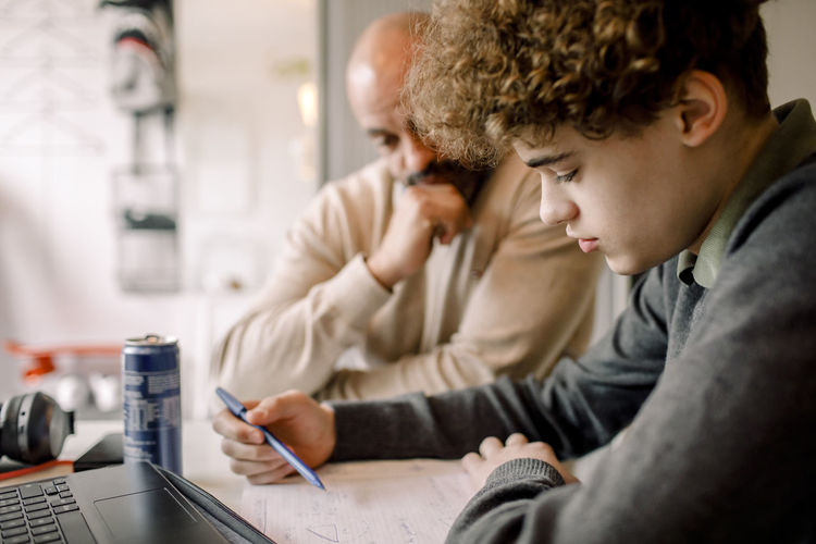 Boy doing homework while sitting by father at home