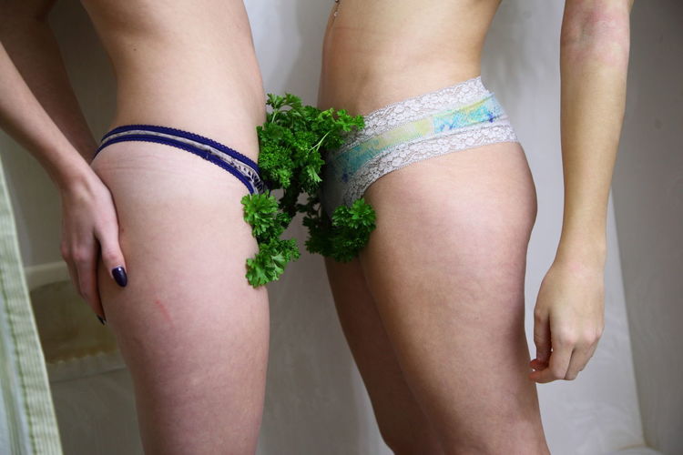 Midsection of female friends with cilantro in panty standing against wall