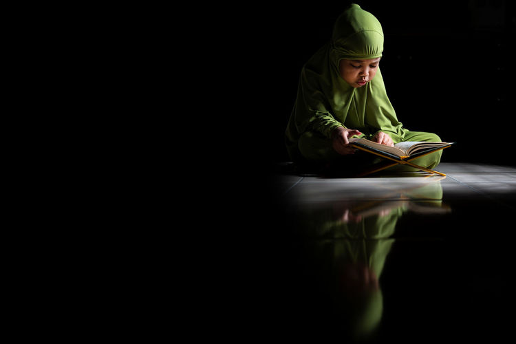 Girl reading koran while sitting on floor in darkroom
