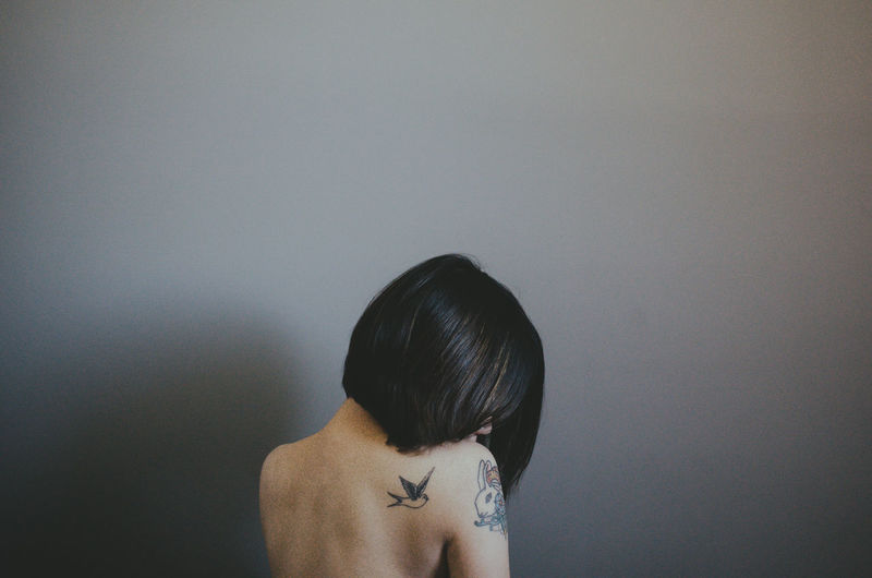 Rear view of shirtless woman against gray wall