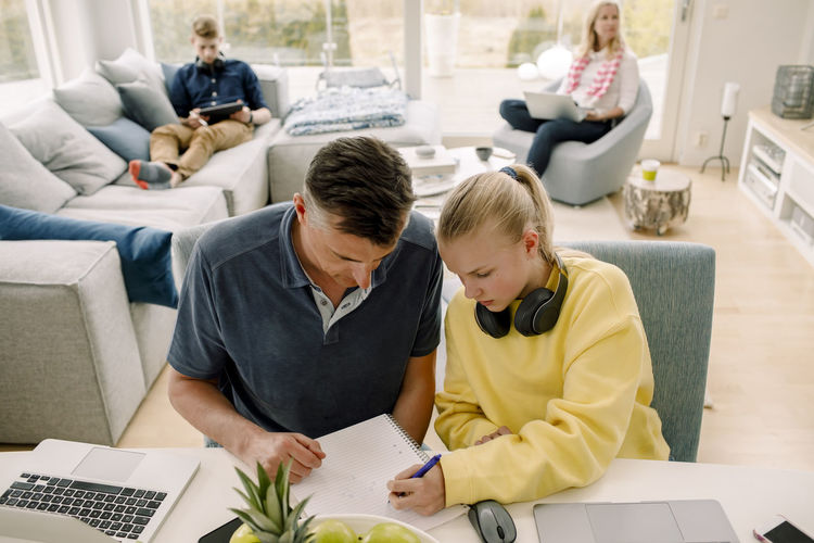 High angle view of father teaching daughter while sitting at table in living room