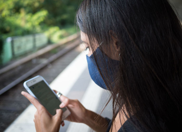 Side view of woman using smart phone sitting on railroad platform