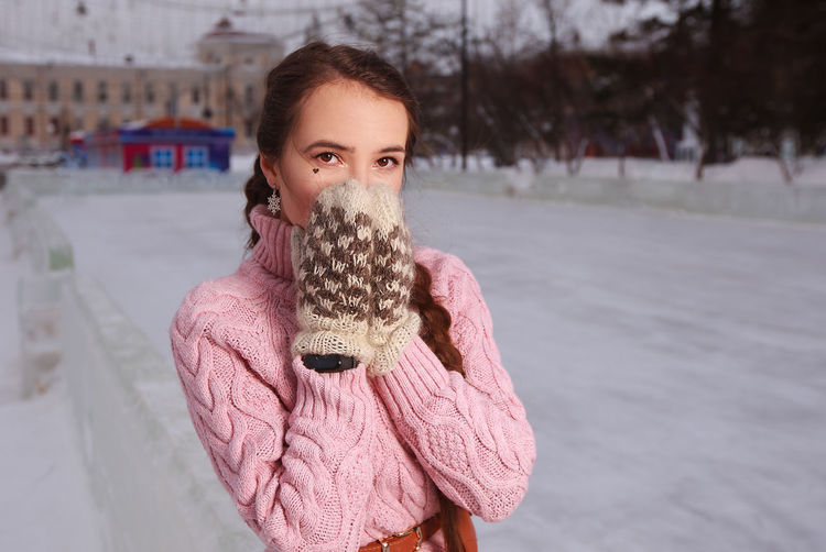 Young woman in pink winter overall combs stands at open air outdoor ice rink