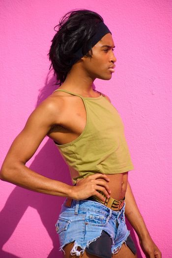 Side view of young model with hand on hip standing against pink wall