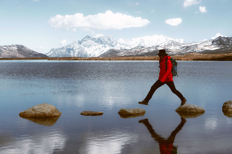 Man walking on stepping stones in lake against snowcapped mountain 