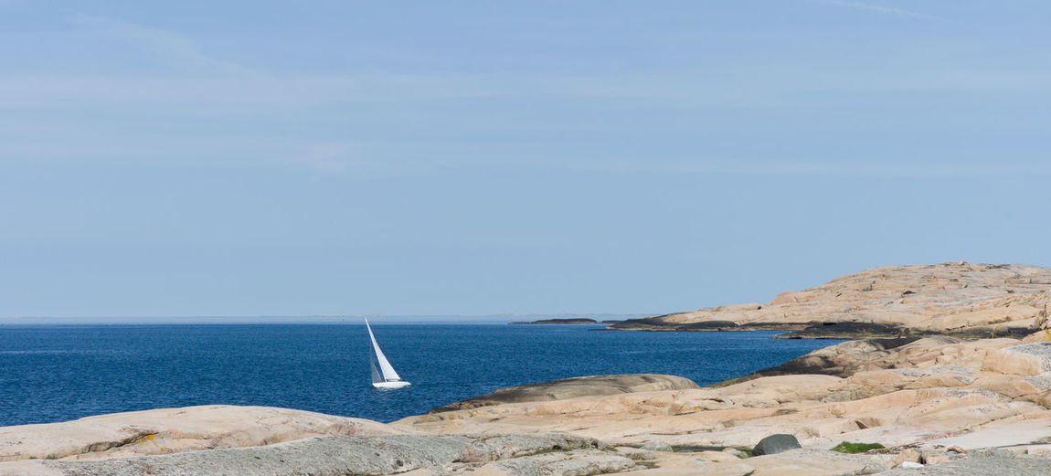 Small sailboat leaning over in the wind near nordic coast landscape