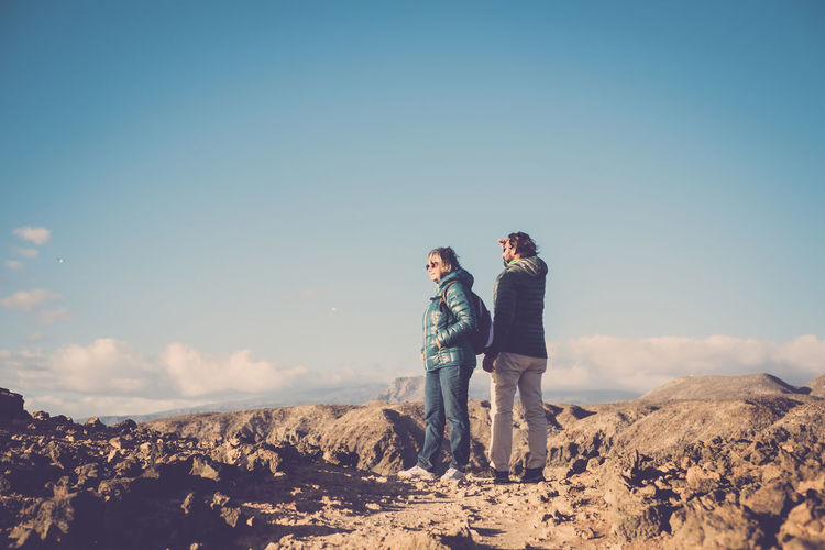 Couple standing on ground against blue sky