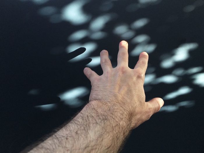 Cropped hand of man reaching for wall with shadows