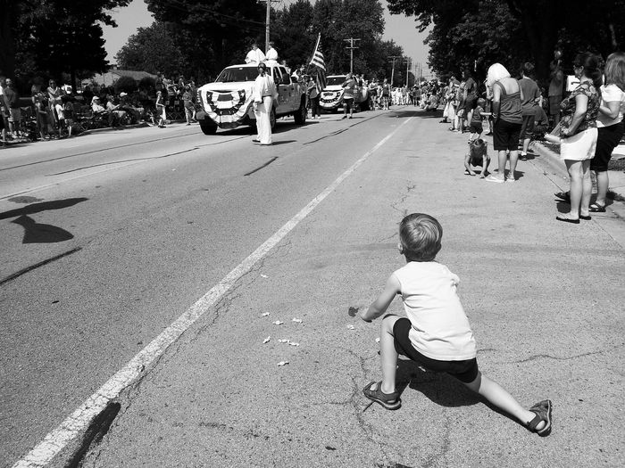Rear view of boy picking up candies from street with parade
