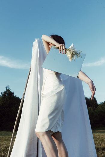 Woman holding umbrella standing on field against sky