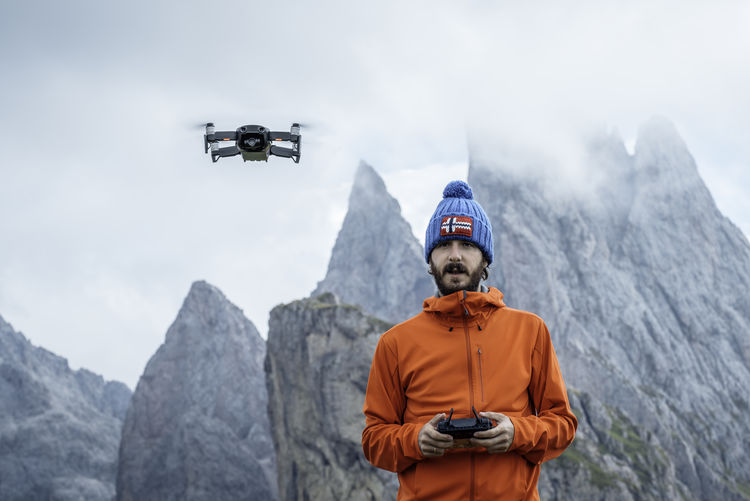 Male traveler with remote controller operating flying drone while standing on background of seceda mountain in italy
