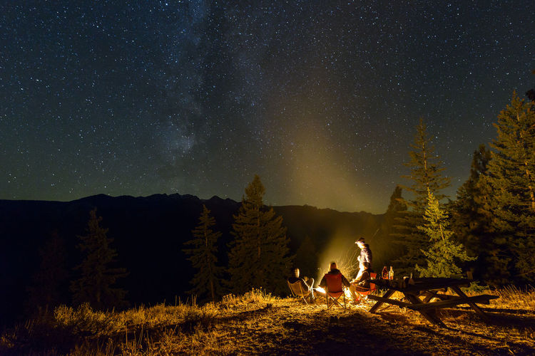 Friends camping on mountain against star field at night