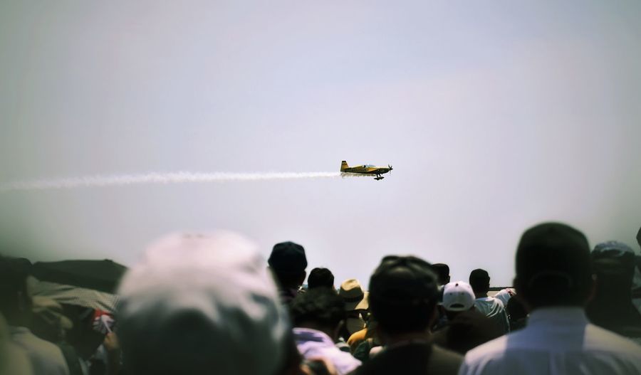 Rear view of people looking at airshow against sky