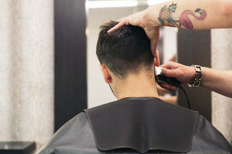 Cropped hands of barber cutting man hair in salon