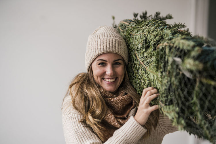Smiling beautiful blond woman carrying christmas tree at home