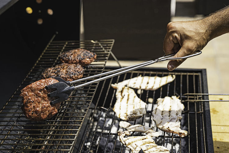 Person holding meat on barbecue grill