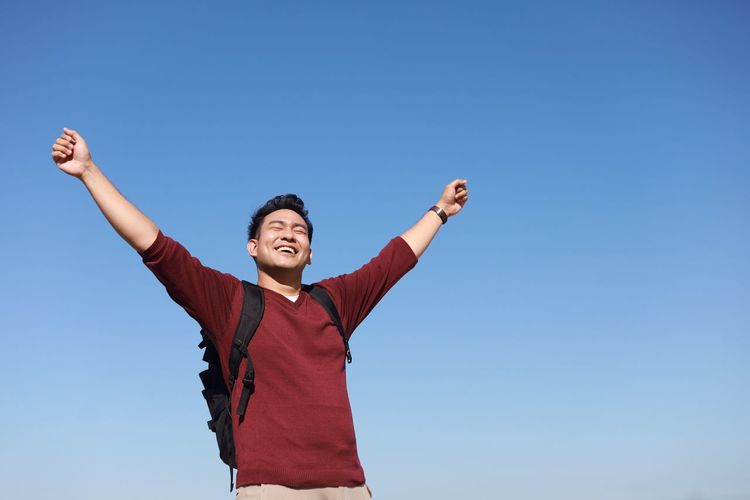Low angle view of happy man standing against clear blue sky