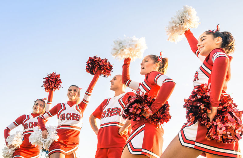 Low angle view of cheerleaders holding pom-poms against clear sky