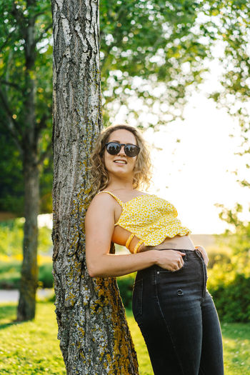 Young woman wearing sunglasses on tree trunk against plants