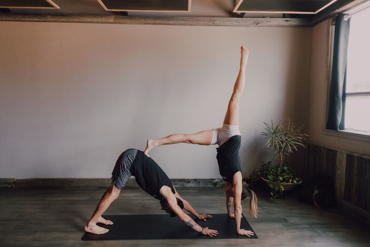 Side view of young barefooted man and focused woman in sportswear doing balance exercise standing in dog pose while training together on floor in light contemporary workout room