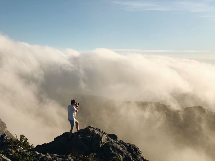 Full length of man photographing landscape against cloudy sky