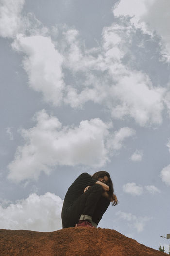 Side view of woman sitting against sky