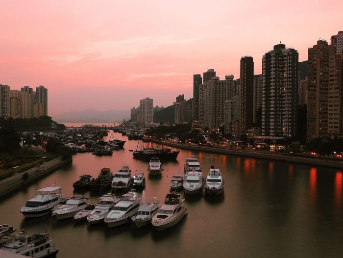 Boats moored on river by buildings against sky during sunset