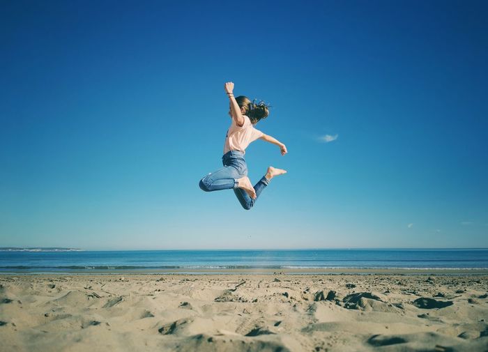 Low angle view of girl jumping on beach against clear blue sky