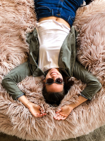 Smiling woman lying on fur cushion wearing sunglasses