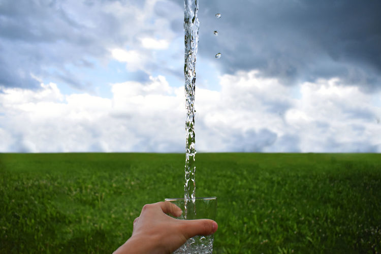 Cropped hand splashing water from glass over field