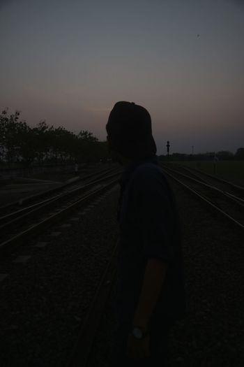 Rear view of man standing on railroad track against sky during sunset