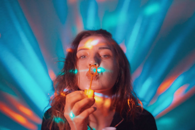 Portrait of woman blowing bubbles against illuminated lights